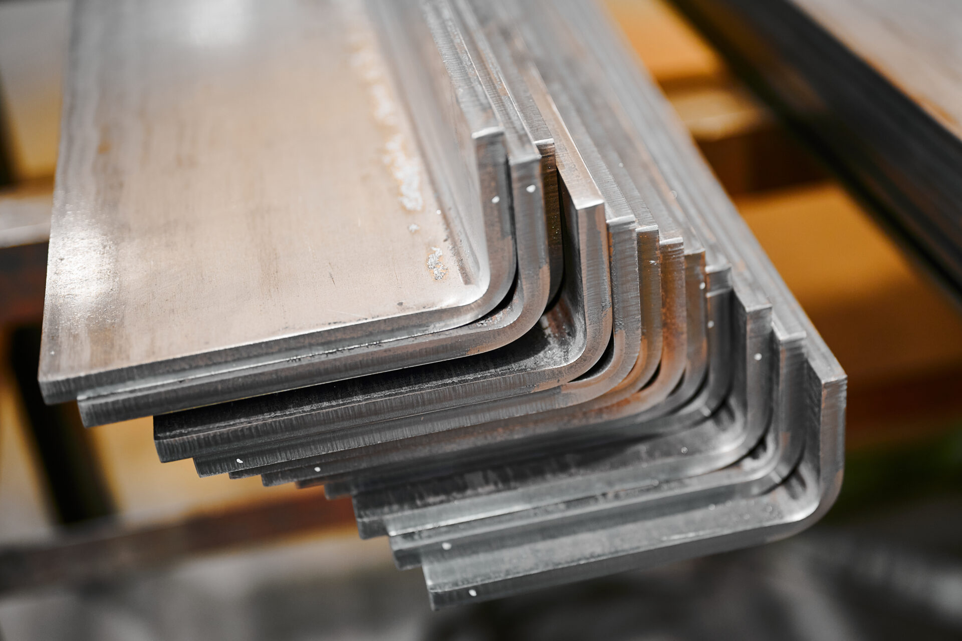 Long bent metal details stacked in production plant storage closeup. Stainless corners at metal rolling plant. Steel workpieces at factory